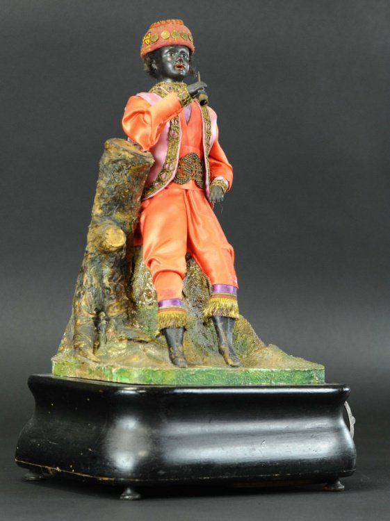 SMOKING PERSIAN STYLE FIGURE AUTOMATON: Clockwork mechanism activates hand and head motions, figure dressed in fancy silk clothing, holds tube pipe in hand, resting on hand painted sculpted branch and rock formation.