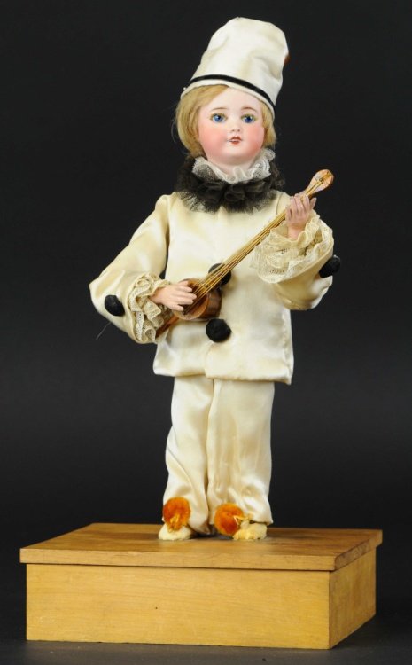 PIERRETTE PLAYING BANJO AUTOMATON: Bisque head figure in full silk attire, holds wooden banjo in hand and appears to strum along to music as clockwork is activated, stands on simple square base with no bottom plate.