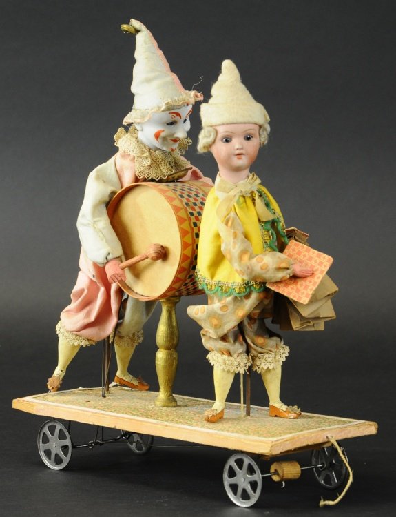 CLOWNS WITH INSTRUMENTS PULL TOY: Amusing toy features two bisque head clowns in full dress standing on wheeled platform, articulated action allows arms to move about as if playing instruments, legs made of wood, drum and accordion ma