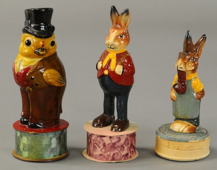 THREE OUTSTANDING EASTER CANDY CONTAINERS: A well dressed Easter chick, red coat bunny and a pipe smoking rabbit wearing a green apron, all on cardboard base candy containers. 5" to 6 1/2".