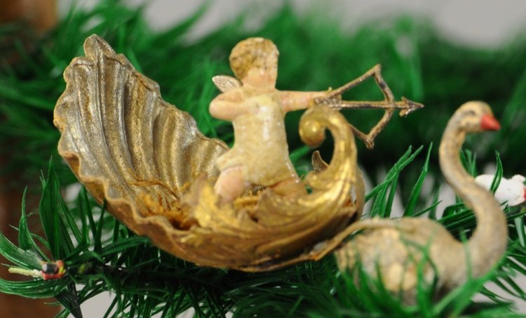 CHERUB IN SWAN PULLED SEASHELL: Cherub has gold wings and bow and arrow, standing in mossy foliage, pulled by tiny swan. 4".