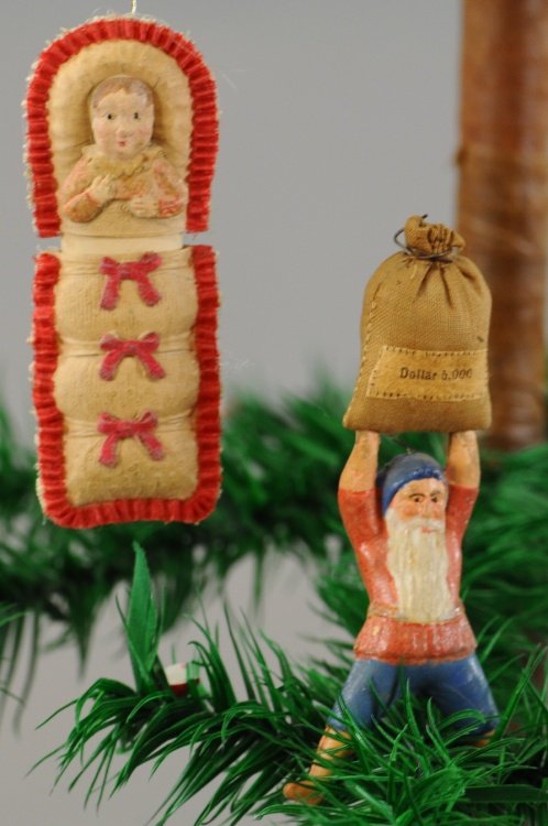 ELF WITH MONEY BAG DRESDEN, BABY IN BUNTING CANDY: Polychrome decorated elf holding canvas $5,000 bag over his head, bunting natural with red ruffles and bows. 3 1/2", 3". Ex. Tom Fox Collection