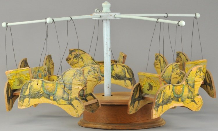 EARLY WOODEN TOY CAROUSEL: Very rare and early example, attributed to Morton Converse, clockwork mechanism concealed within wooden base, features five die cut pony gondolas, each done in lithographed paper on wood construction,