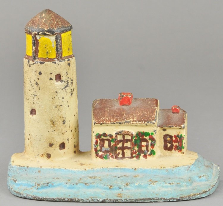 LIGHTHOUSE DOORSTOP: Cast iron lighthouse and keeper's house depicted on beach with shoreline and ocean waves. 6 1/2" h.