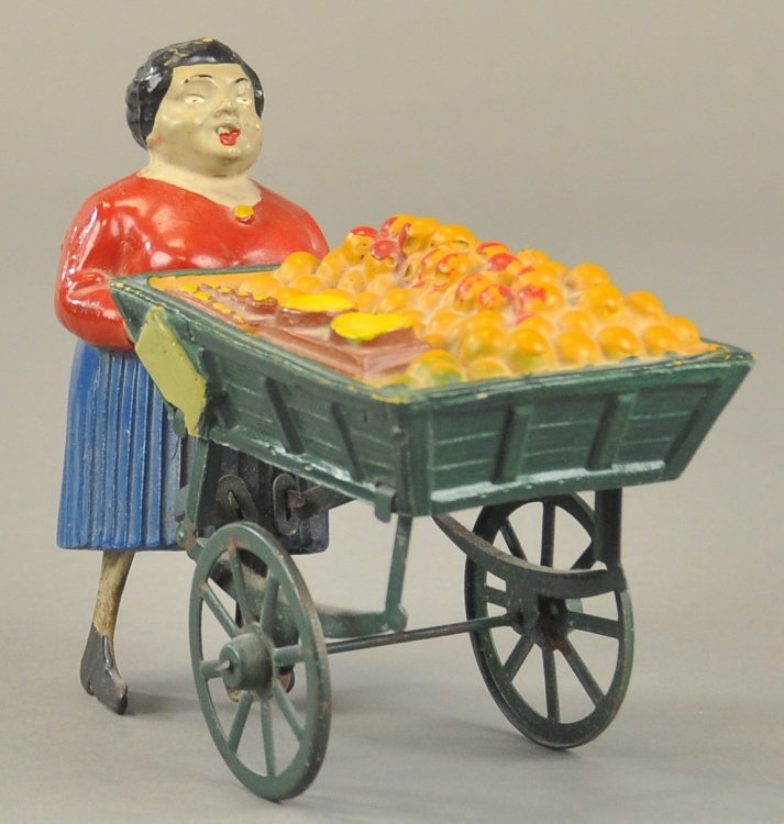 LADY PUSHING FRUIT CART: Maker unknown, attributed to France, made of composition and hand painted, embossed vending wagon contains fruit piled high in open wagon, clockwork activates legs for motion, spoke wheels. 6" l.