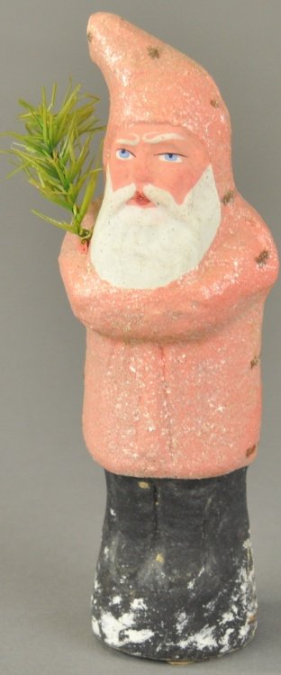 * SMALL PINK ROBE BELSNICKLE: Germany, pressed and stapled cardboard, this Santa holds a feather tree sprig while standing on a snow covered tree stump. 6 1/2" h.
