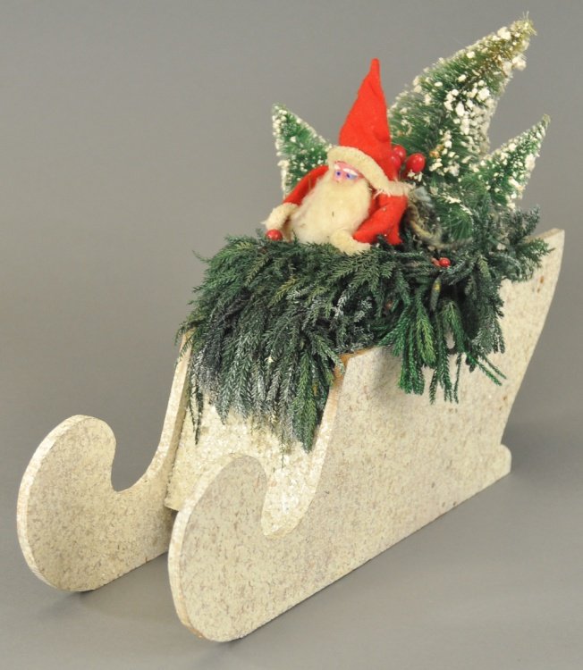 SANTA IN MUSIC BOX SLEIGH: Santa sits atop a mica flecked sleigh, composition head with cotton beard, surrounded by lichen moss and bottle brush trees, music box plays jingle bells. 14" h.