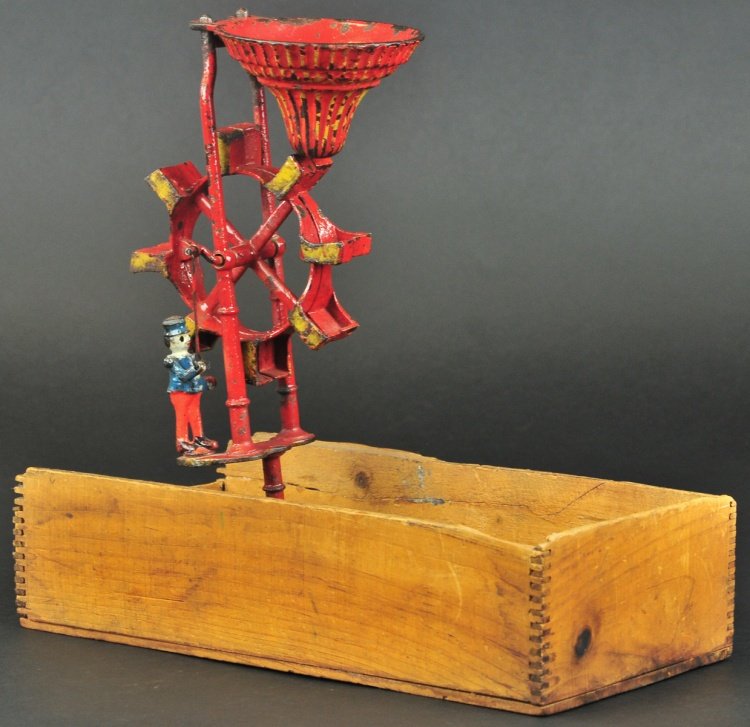 IVES EXCELSIOR SERIES SAND TOY WITH BOX: Rare, cast iron, painted in red overall with gold highlighter, as sand pours from removable hopper, bucket catches and releases sand and spins, standing figures arm is attached to articulated lever ma