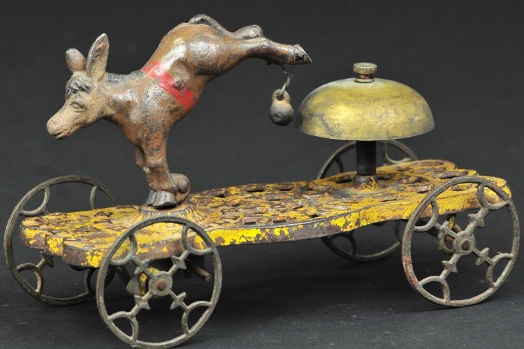 GONG BELL DONKEY BELL TOY: No. 42, hand painted cast iron, yellow base, contains donkey figural with articulated axle, able to swing and strike bell, ornate spoke wheels. 7 1/2" l.