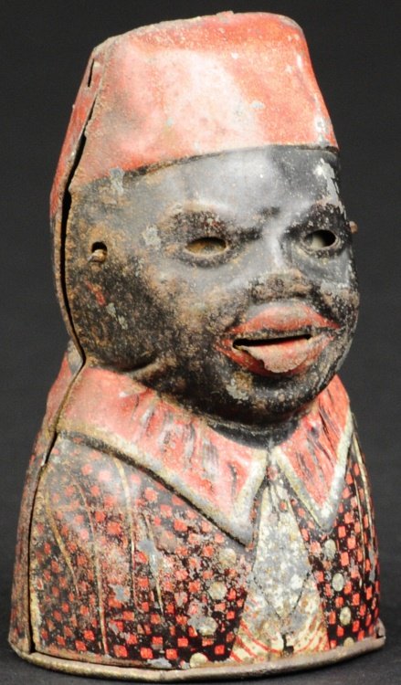 DARKY TIN BUST MECHANICAL BANK: Mfg. by Maienthau & Wolf, Germany, circa 1907, rare tin lithographed example, familiar coin action allows tongue to protrude and eyes to roll when deposit is made. Provenance: Edwin H. Mosler Jr. Coll