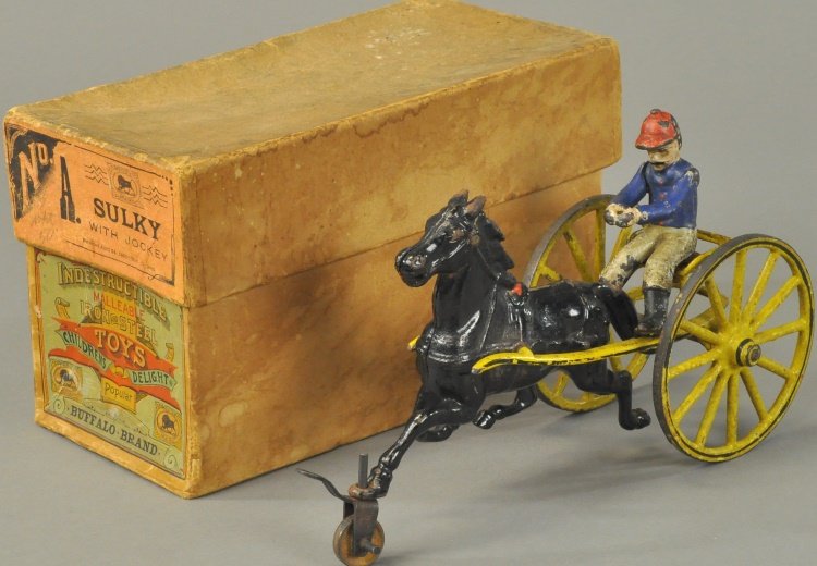 BOXED PRATT & LETCHWORTH SULKY: Cast iron, yellow sulky, embossed seating, large spoke wheels with gold trim, seated jockey, drawn by black horse, includes scarce box with "Buffalo Toy" brand name. 8" l.Note: Includes front leading