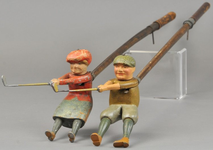 LOT OF TWO SCHOENHUT GOLFERS: Includes lady golfer in red dress and gentleman in green & grey; both are wood carved bodies that hold a silver club in hands, attached to a wooden stick with lever that allows golfer to swing and tur