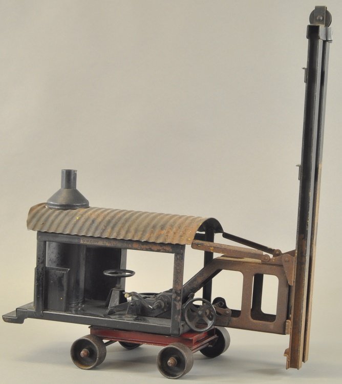 BUDDY 'L' PILE DRIVER ON WHEELS: c. 1920's, pressed steel, frame and support painted in black, vertical boiler on base, corrugated red roof and wheeled platform, contains tall driver once used with weight. 22" h. x 19" l.