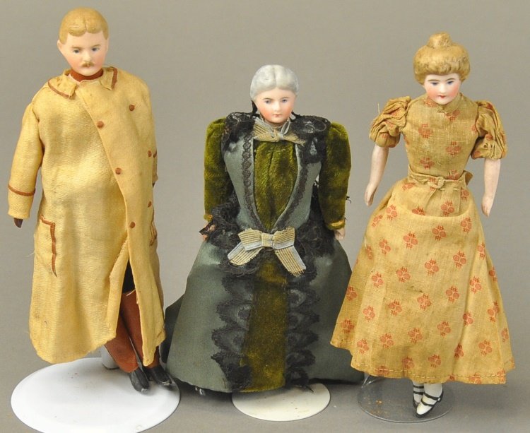 LOT OF THREE DOLLHOUSE DOLLS: Lady has blond molded hair pulled up in bun, dressed in original beige and pink flowered dress with black heeled shoes, original clothing gentleman in long beige coat trimmed in rose color, long pants