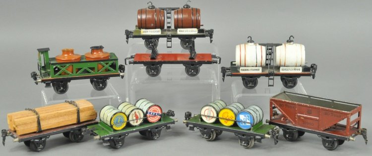 MARKLIN FREIGHT CARS: O' gauge car lot, four wheel examples include: lumber car, stake car, wine car with two white barrels, oil barrel carriers, acid car with brake-house, wine car with two brown barrels and hopper. 6 1/2