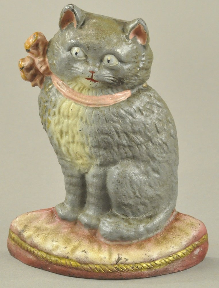 CAT ON CUSHION DOORSTOP: Features a beautiful grey and white cat sitting tall on pink cushion base, excellent casting details with blue eyes and pink bow to match cushion. 8" l.