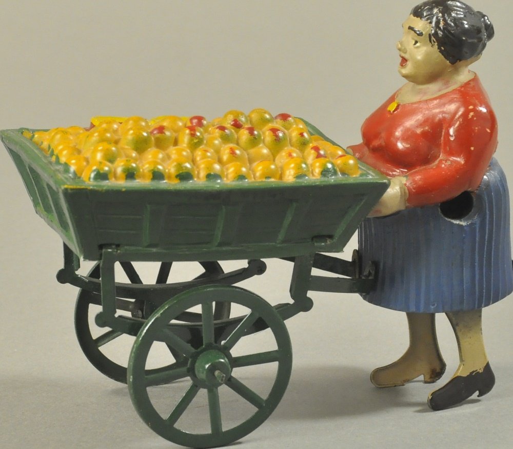 WOMAN PUSHING FRUIT CART: Maker unknown, attributed to France, made of composition and hand painted, embossed vending wagon contains fruit piled high in open wagon, clockwork activates legs for motion, spoke wheels. 6" l.