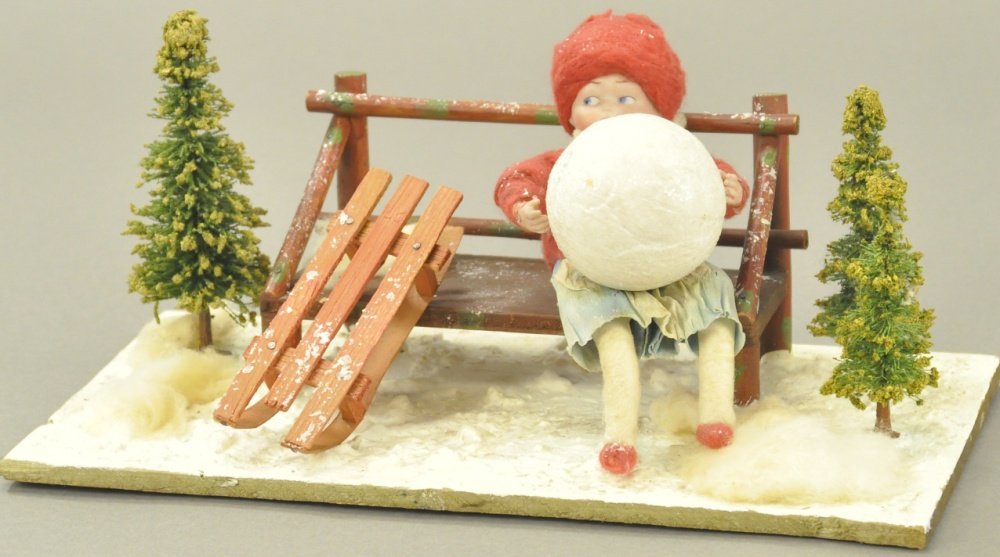 HEUBACH GIRL w/SNOWBALL: A wonderful depiction of spun cotton batting girl with Heubach face, red coat and hat, sitting on bench holding giant snowball, an impressive winter image. 11" l.