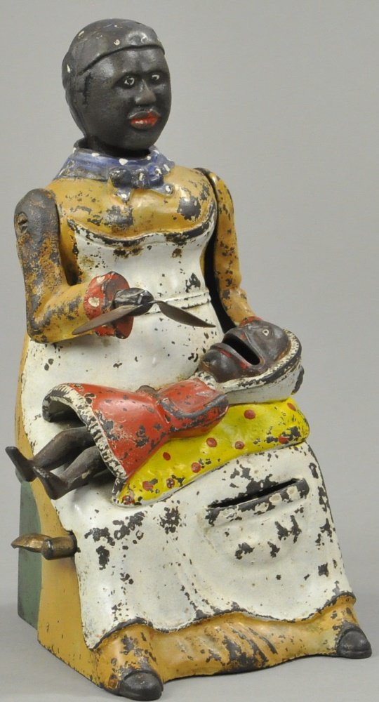 MAMMY AND SPOON MECHANICAL BANK: Beige dress version, Kyser & Rex Mfg., circa 1884, place coin in slot at the knee of mammy’s apron and press the lever, mammy lowers her spoon as if feeding the baby and her head lowers, the baby’