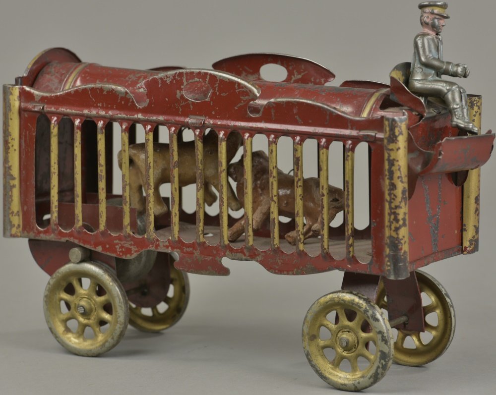SCHIEBLE CIRCUS WAGON: circa 1911, pressed steel and painted in red, cage body houses two composition animals, gold spoke wheels, opening rear door, scarce example with seated driver. 13" l.