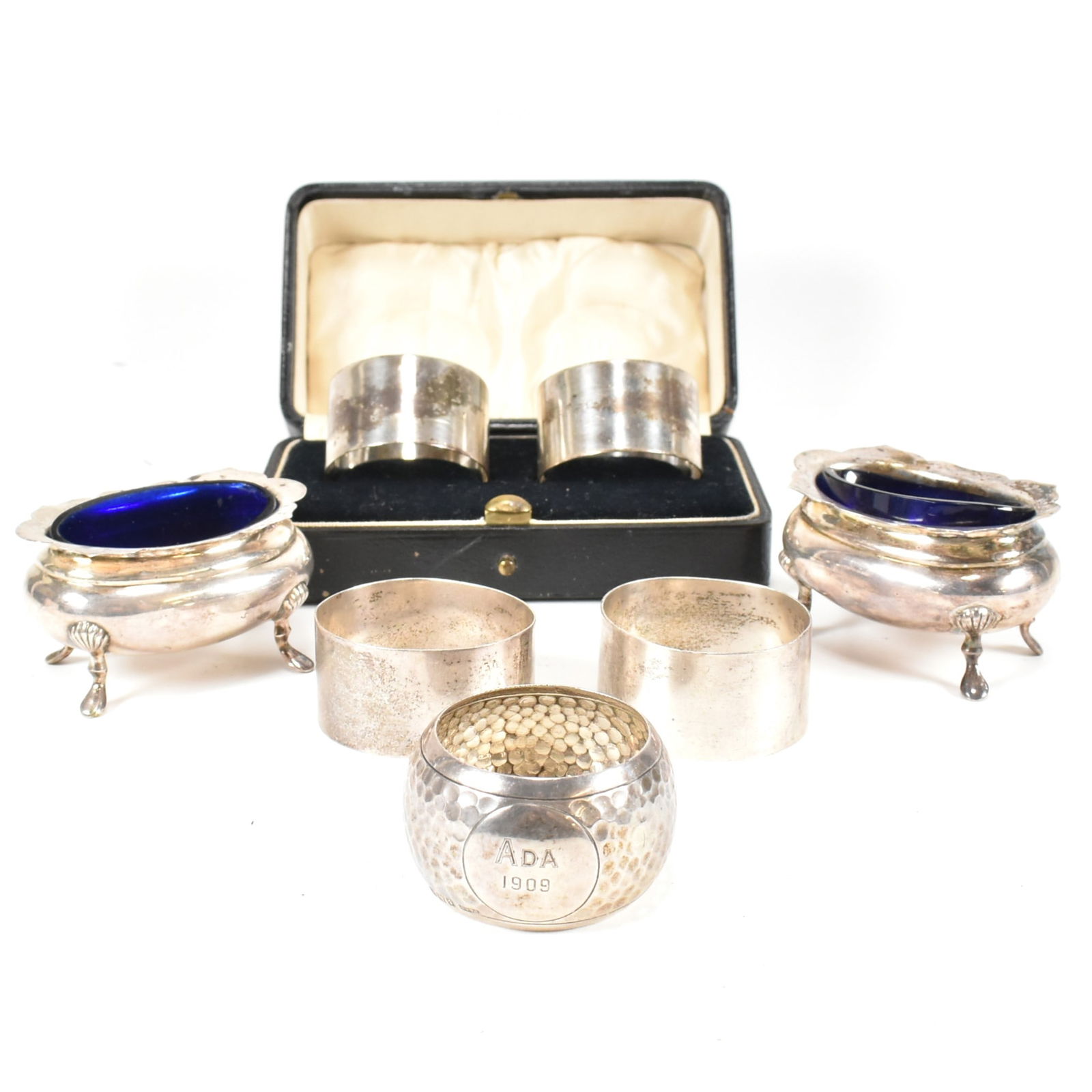 PAIR OF GEORGE V HALLMARKED TABLE SALTS & COLLECTION OF NAPKIN RINGS TBV: A pair of George V hallmarked silver blue glass lined table salts. Hallmarked Sheffield 1920. Sponsors mark for Henry Williamson. Weight exc liners 87g. Together with a cased set of hallmarked silver