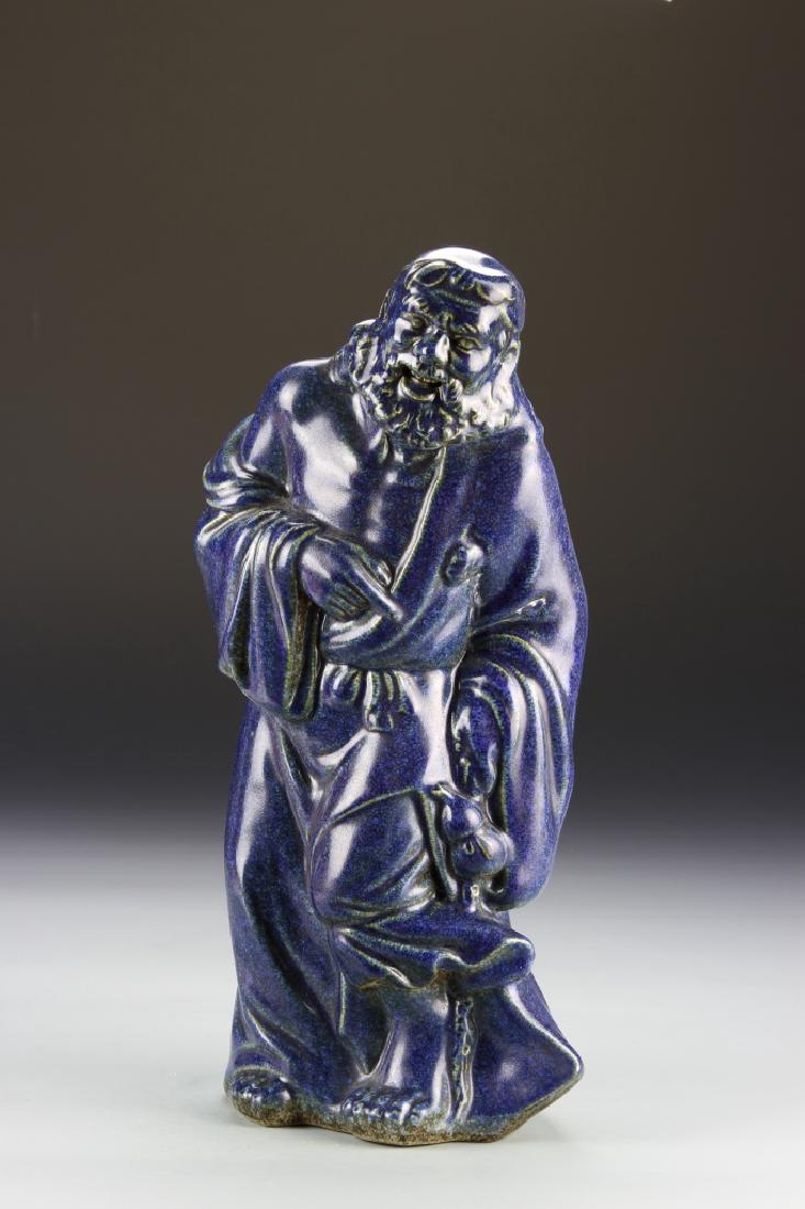 Chinese Blue Glazed Figure: China, blue figure, in a relaxed standing form, wearing a flowing robe, with an intricately carved beard and facial details, painted in a deep blue glaze with flat base. Height 14 in.