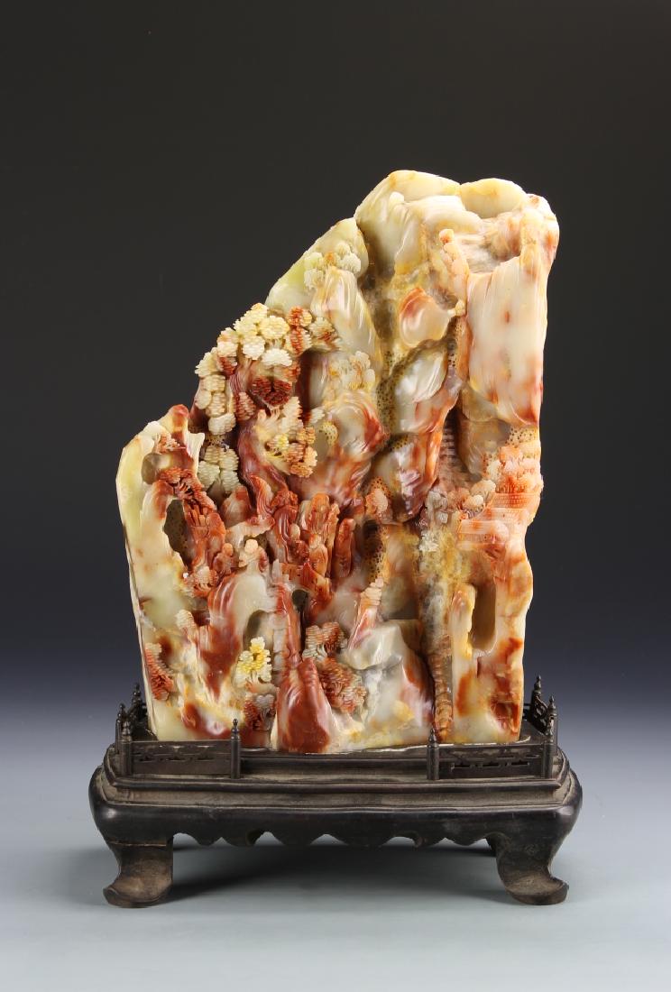 Chinese Shoushan Mountain: China, carved Shoushan mountain, with intricately carved details, in a mottled red-brown hue, with striations in the stone, on wooden base with four legs. Height 12 in.