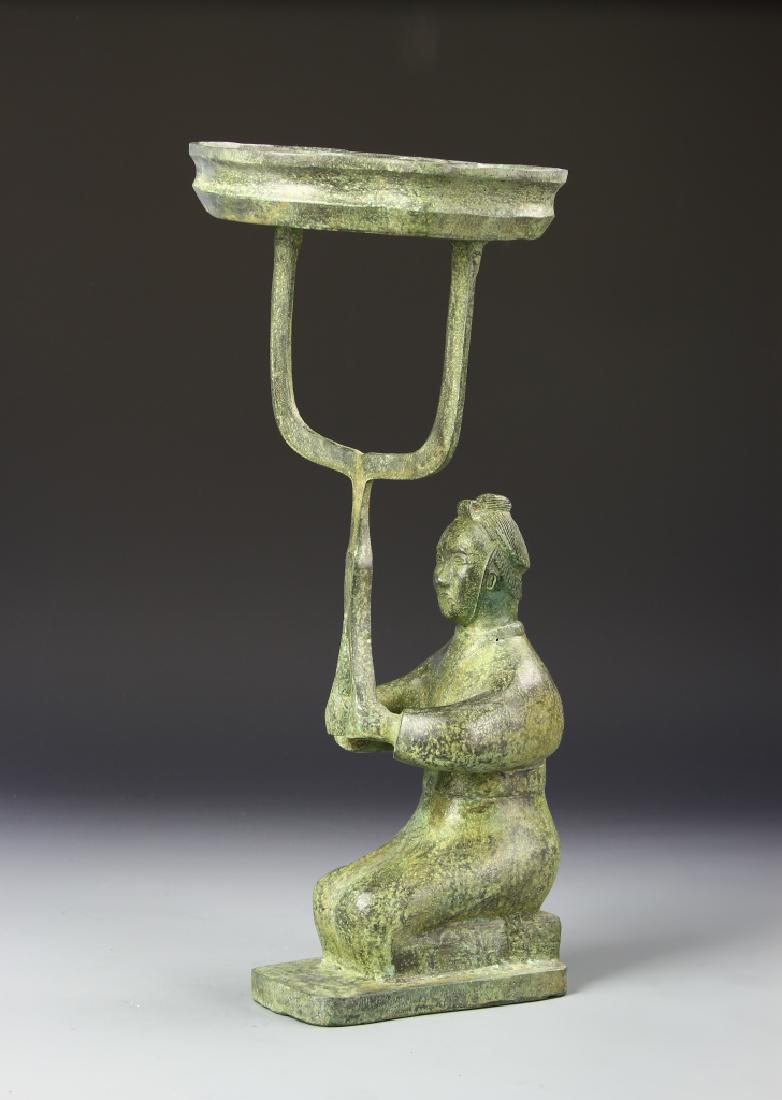 Chinese Bronze Lantern: China, antique bronze lantern, simplistic carving of a male figure, kneeling on the ground and holding up a speared shape, with patina throughout and flat base. Height 16 in.