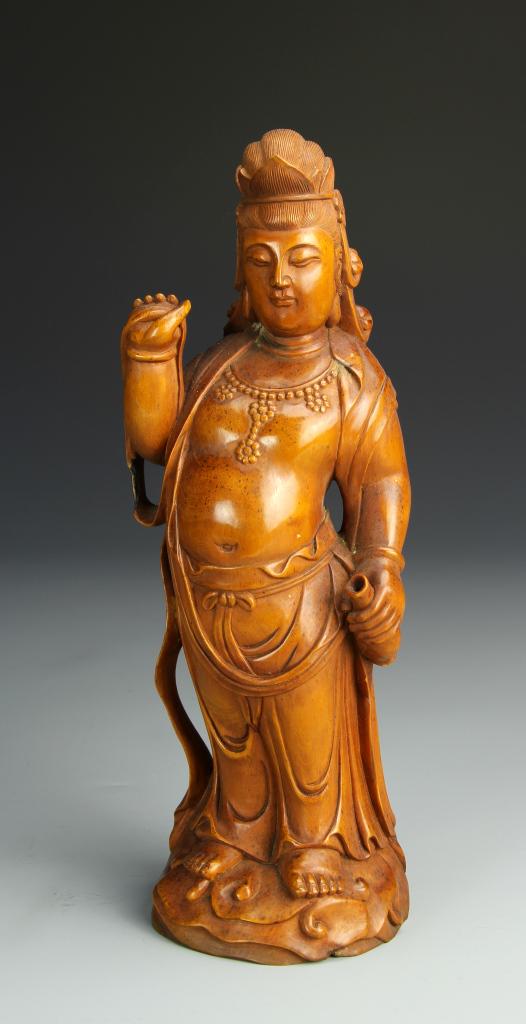 Chinese Carved Boxwood Guanyin: China, carved boxwood figure of Guanyin, rich honey color with carved details, standing figure as though on waves, holding simple robes in one hand and a vase in the other. Height 9 1/2 in.