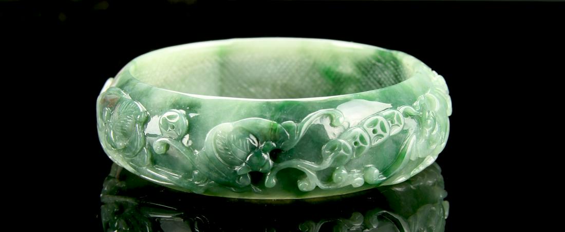 Chinese Jadeite Bangle: China, jadeite bangle, with intricately carved floral motifs, in a deep green hue, with striations in the stone, and a high shine surface. Diameter 2 7/8 in.