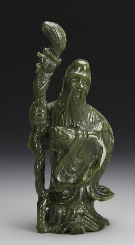Chinese Carved Jade Figure: China, carved jade figure, moss green stone with flecks of black, expert carving detailing an elderly figure with long beard and robes holding a large scepter. Height: 7 in.