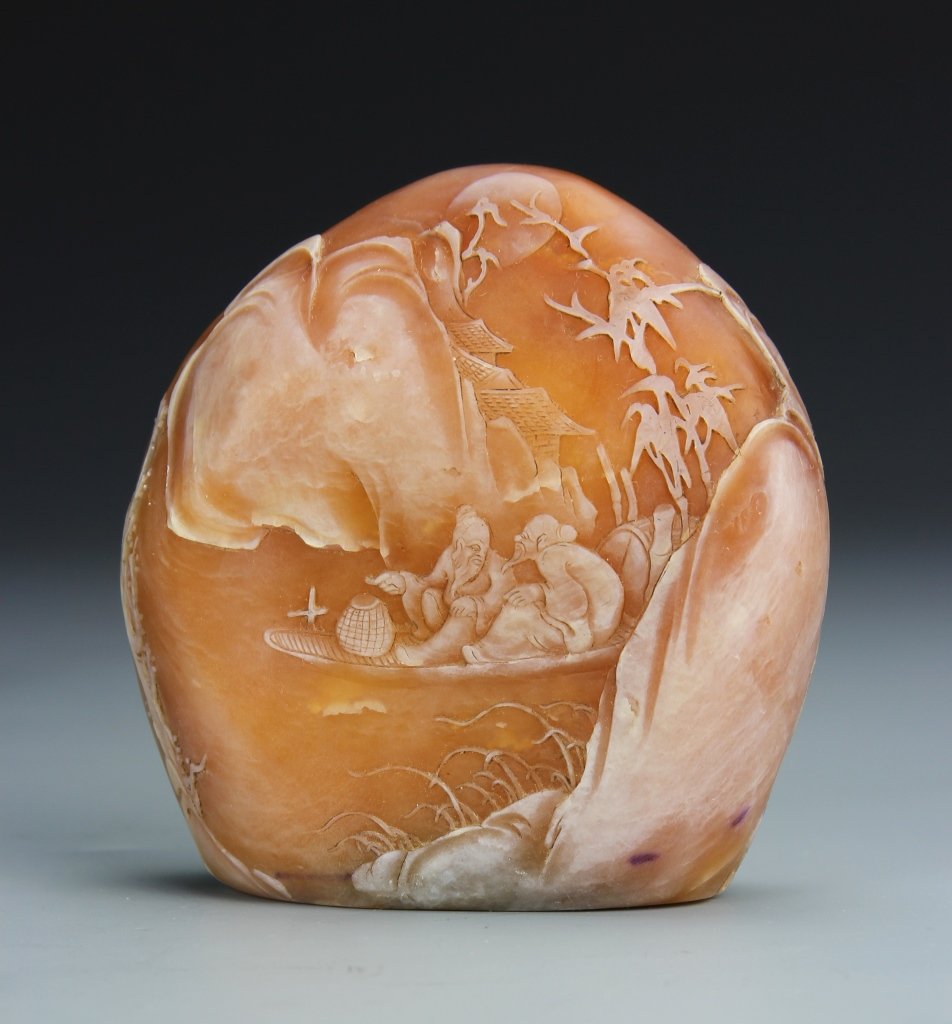 Chinese Carved Soapstone Boulder: China, carved soapstone boulder, organic form and color, marked in white with a continuos scene showing two figures on a boat drifting by mountains, trees and homes with the moon above the clouds. Len