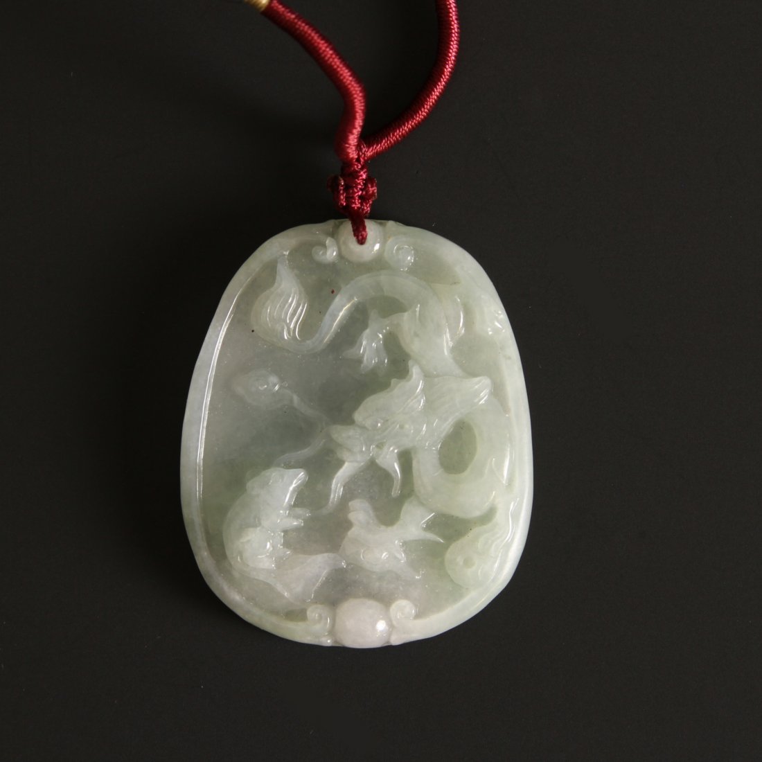 Chinese Carved Jadeite Pendant: China, jadeite pendant in an ovoid form, carved with a chi dragon design, and pierced for hanging. Height 2 in.