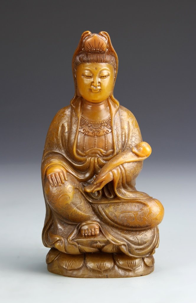 Chinese Shoushan Stone Buddha Figure: China, carved variations of yellow Shoushan stone figure of Buddha seated upon a lotus flower, with flowing robs, a highly adorned head piece, and holding a scroll. Height 7 1/4 in.