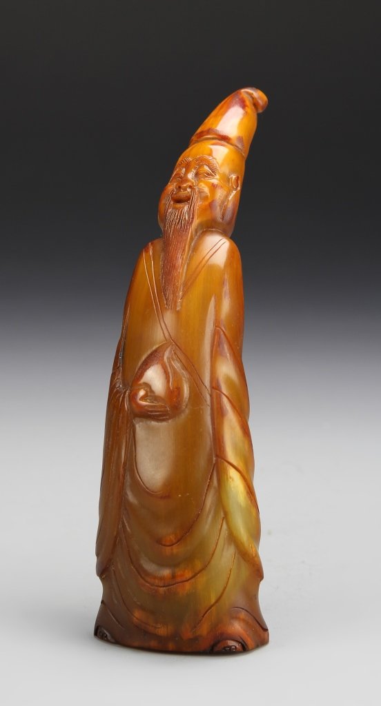 Chinese Carved Horn Man Figure: China, carved horn man figure, leaning back with carved robe and headpiece, orange in color. Dimensions 7 in.