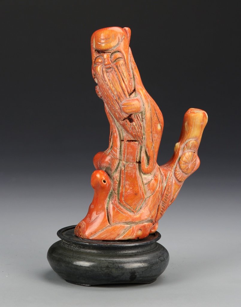 Chinese Carved Coral Man Figure with Base: China, 19th C., carved coral man, in the form of coral, man sits on a low tree branch, stylized beard, minimally carved robe and facial features, with small circular wooden base. Height 4 1/2 in.