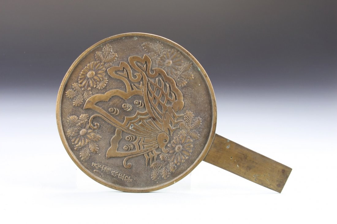 Japanese Bronze Mirror: Japan, bronze mirror, in circular form, with handle, large butterfly motif across thew surface, with scrolling floral details in the background. Height 10 3/4 in.