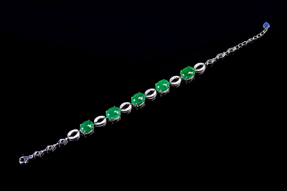 Chinese Jadeite Bracelet: China, jadeite bracelet, with ovular stones, in a deep green hue, set in a metal setting with ovular formed links, and a geometric chain. Length 8 in.