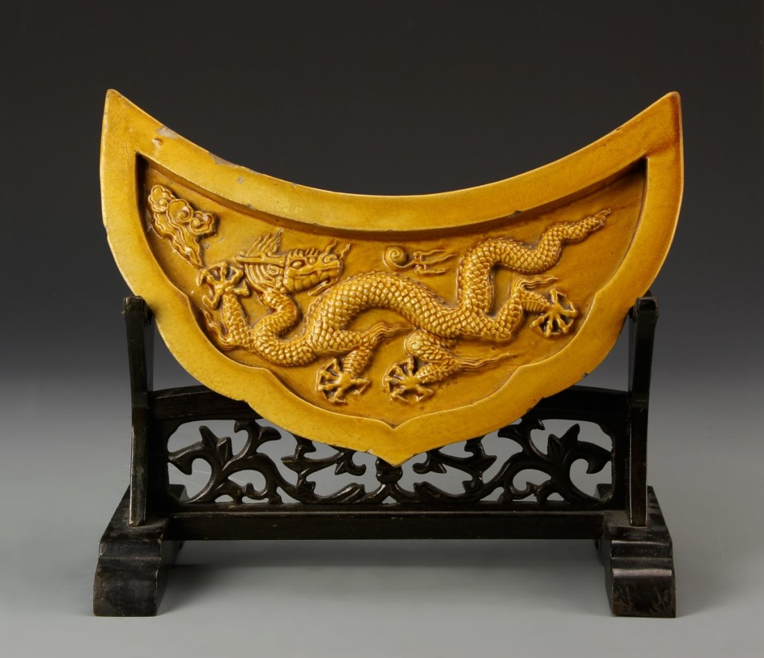 Chinese Ming Period Yellow Tile: China, Ming Period, yellow tile, in the shape of the crescent moon, decorated with a serpentine five-clawed dragon amidst stylized clouds and flaming pearls, with stand. Width 12 in., Height 6 3/4 in.