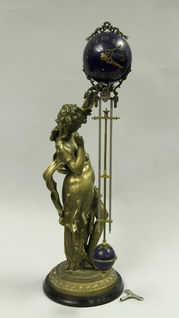 French Mystery Clock: France, a mystery clock, the clock face a bright blue colors with Arabic numerals and minute and hour hands, leading down and terminating in a smaller blue pendulum, all held by the bronze sculpture o