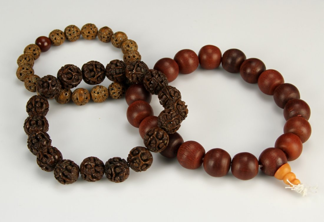Three Chinese Bracelets: China, three bracelets, two Puti seed bracelets, intricately carved, in brown hues, and one wood bracelet, with cylindrical beads, and wood grain showing. Overall Length of the longest, 14 in.