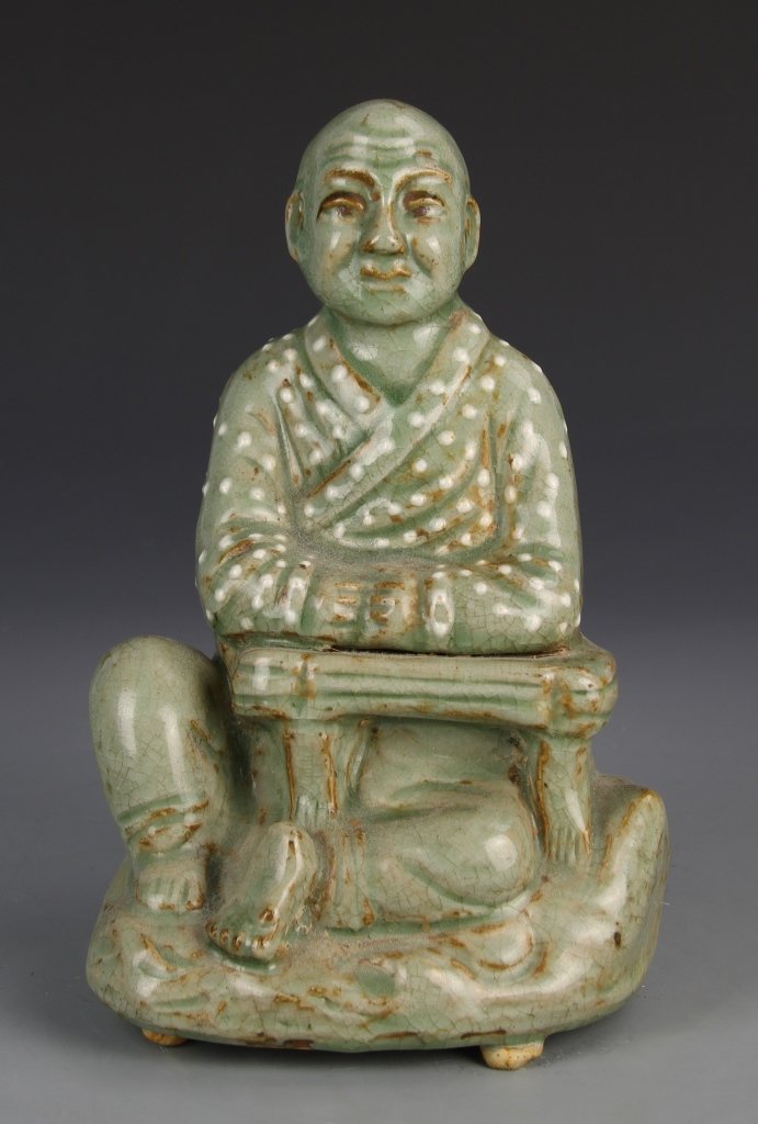 Chinese Lungquan Ware Buddha: China, Lungquan ware Buddha, in a seated position with crossed legs underneath a desk, the robes decorated with a speckled design, detail in the serene face and wrinkled forehead. Height 9 in.