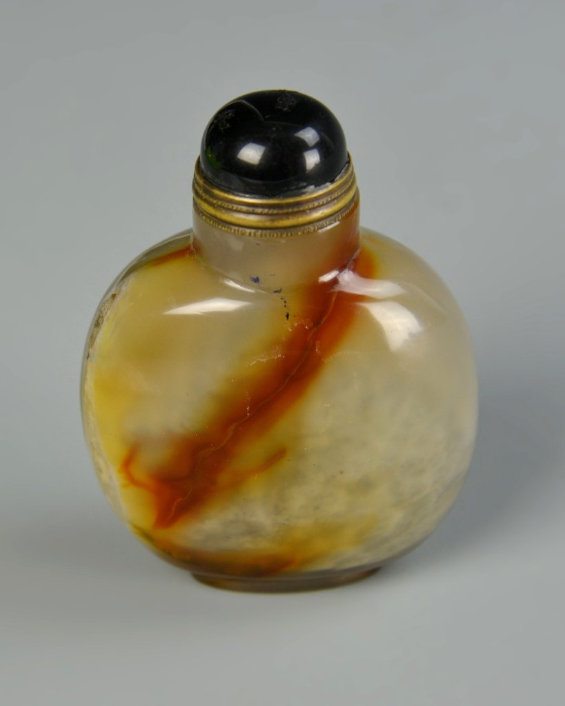 Chinese Agate Snuff Bottle: China, 19th C., agate snuff bottle, in a flattened globular form, clear/white in hue with a large brown striation diagonally through the body, with blue stopper. Height 3 in.