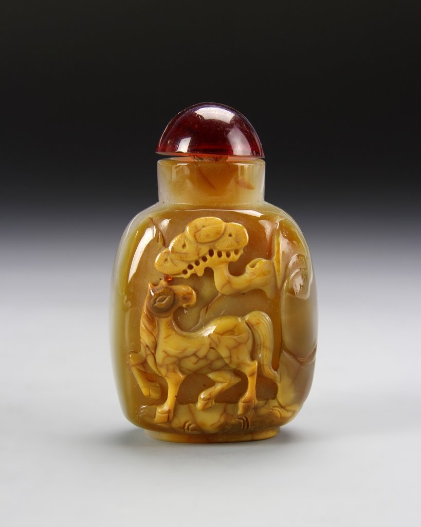 Chinese Agate Snuff Bottle: China, agate snuff bottle, flattened square form, with raised relief design on front of a horse under a tree, in a yellow mottled hue, with large rounded red stopper. Height 2 3/4 in.