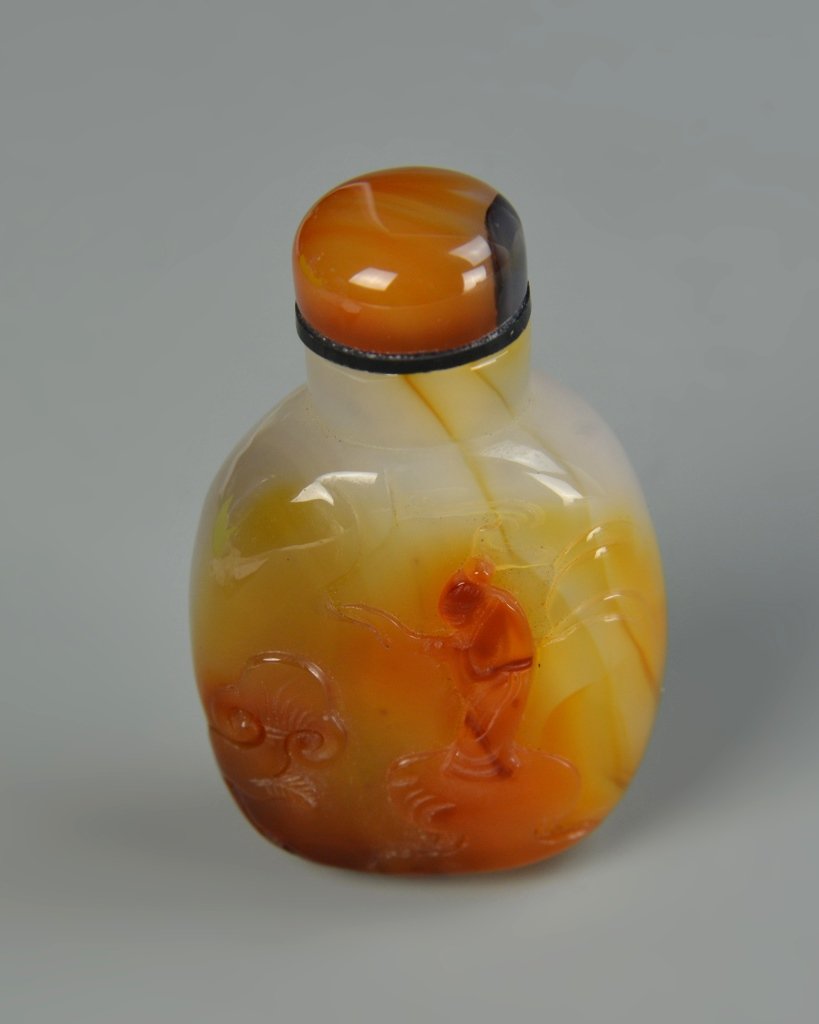 Chinese Carved Agate Snuff Bottle: China, 19th C., carved agate snuff bottle, in a flattened ovular form, with a variety of light brown and red hues, with the image of a figure. Height 2 5/8 in.