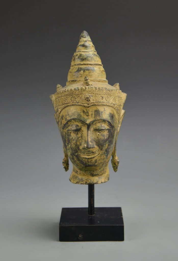 Thailand Antique Bronze Head: Thailand, antique bronze head, simplistically carved faced, with closed eyes, elongated ears, and headpiece in the form of a cone. Height 10 in.