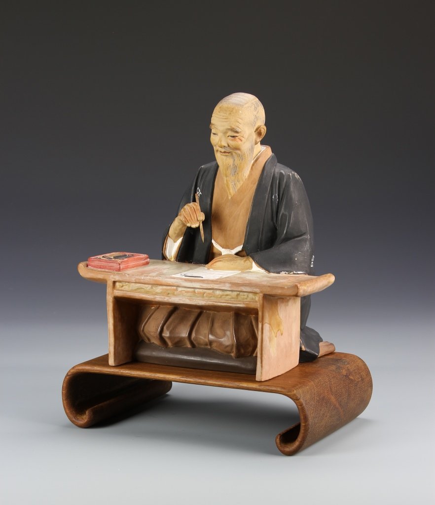 Chinese Pottery Scholar with Base: China, pottery scholar, in a seated position, at a table, holding a brush, dressed in deep blue robes, with wood base. Height 9 in.
