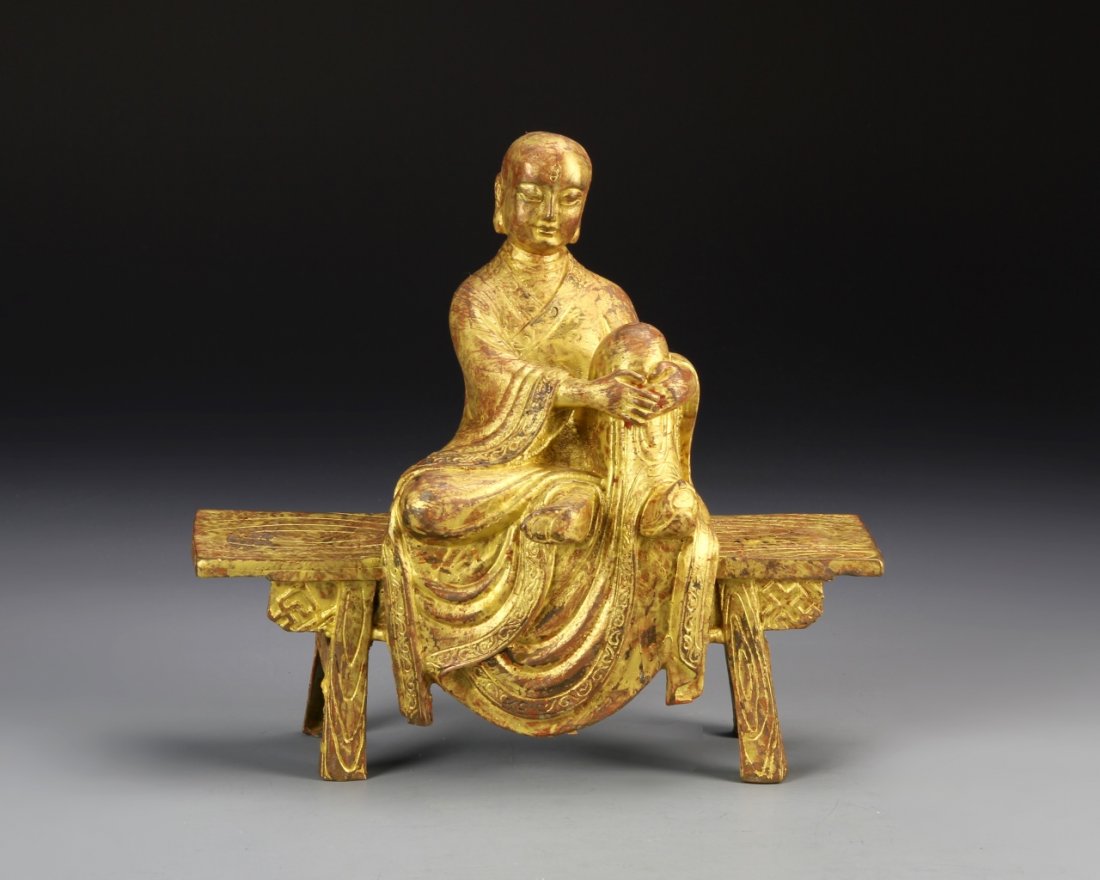 Chinese Gilt Buddha: China, gilt Buddha, on bench, in a seated position, with arms wrapped around upright knee, wearing a flowing robe, with geometric pattern. Height 8 in., Width 8 in.