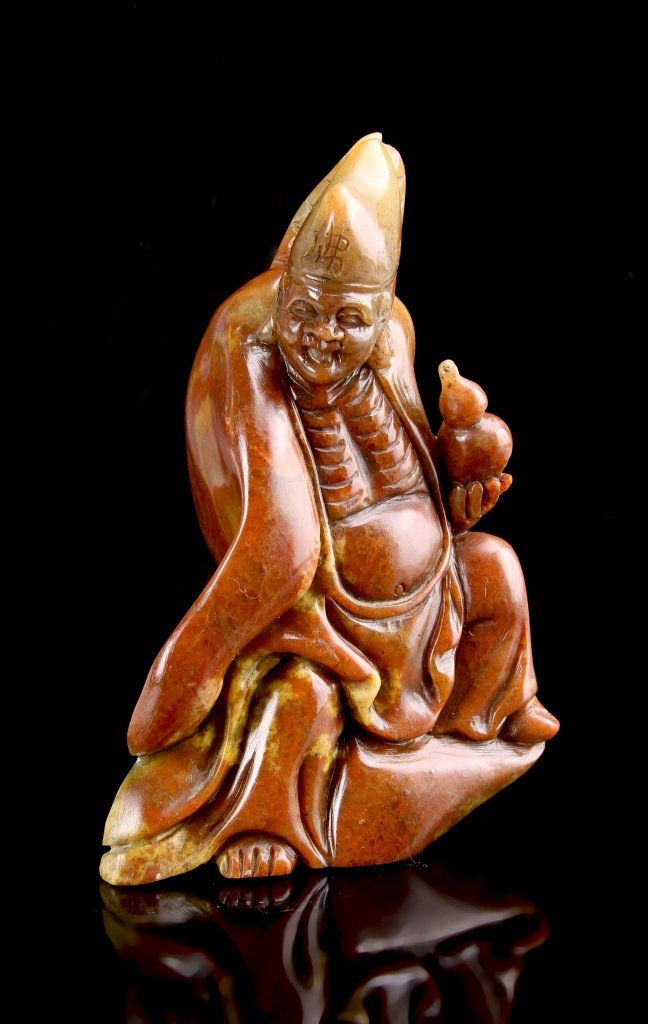 Chinese Carved Shoushan Buddha: China, 19th C., carved Shoushan stone Buddha Ji Geng figure, in a seated position, holding a double gourd object in hand, wearing a flowing robe, with a cone formed head. Height 6 1/4 in.