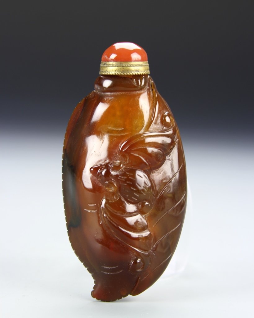 Chinese Agate Snuff Bottle: China, 19th C. carved agate snuff bottle, with bat motifs carved into the outer surface, in mottled hues of brown with reddish-orange stopper. Height 3 1/2 in.